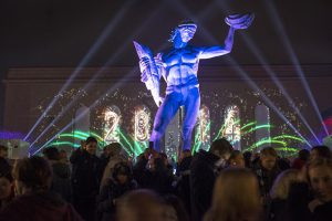 Färgglada strålkastare lyser upp Posiedon-statyn i mörkret. Runt om står en massa människor.