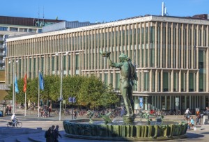 Folk i rörelse runt Poseidon-statyn och Stadsbiblioteket vid Götaplatsen.