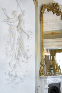 Vit vägg med stuckaturfigurer och spegel med guldram