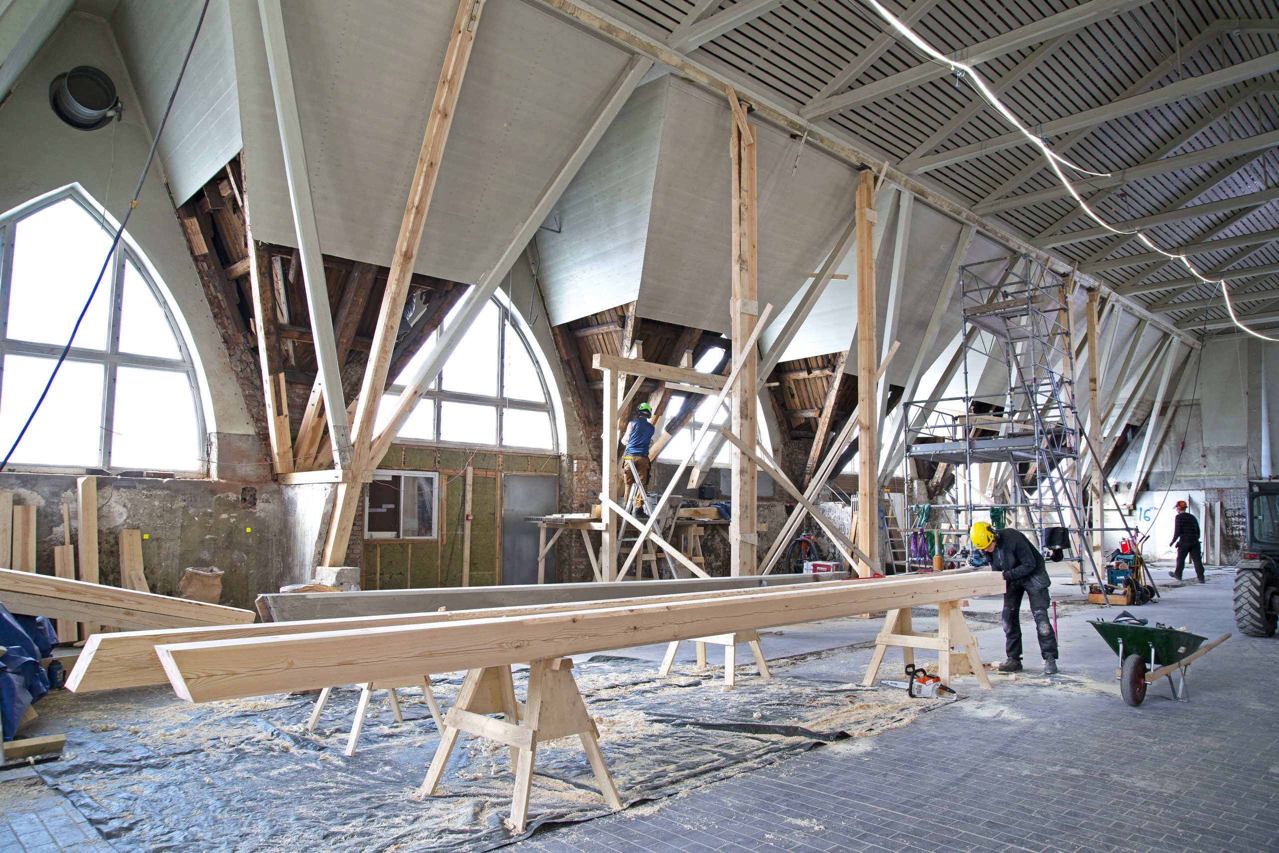 Byggarbetare som arbetar med trä inne i en stor öppen byggnad