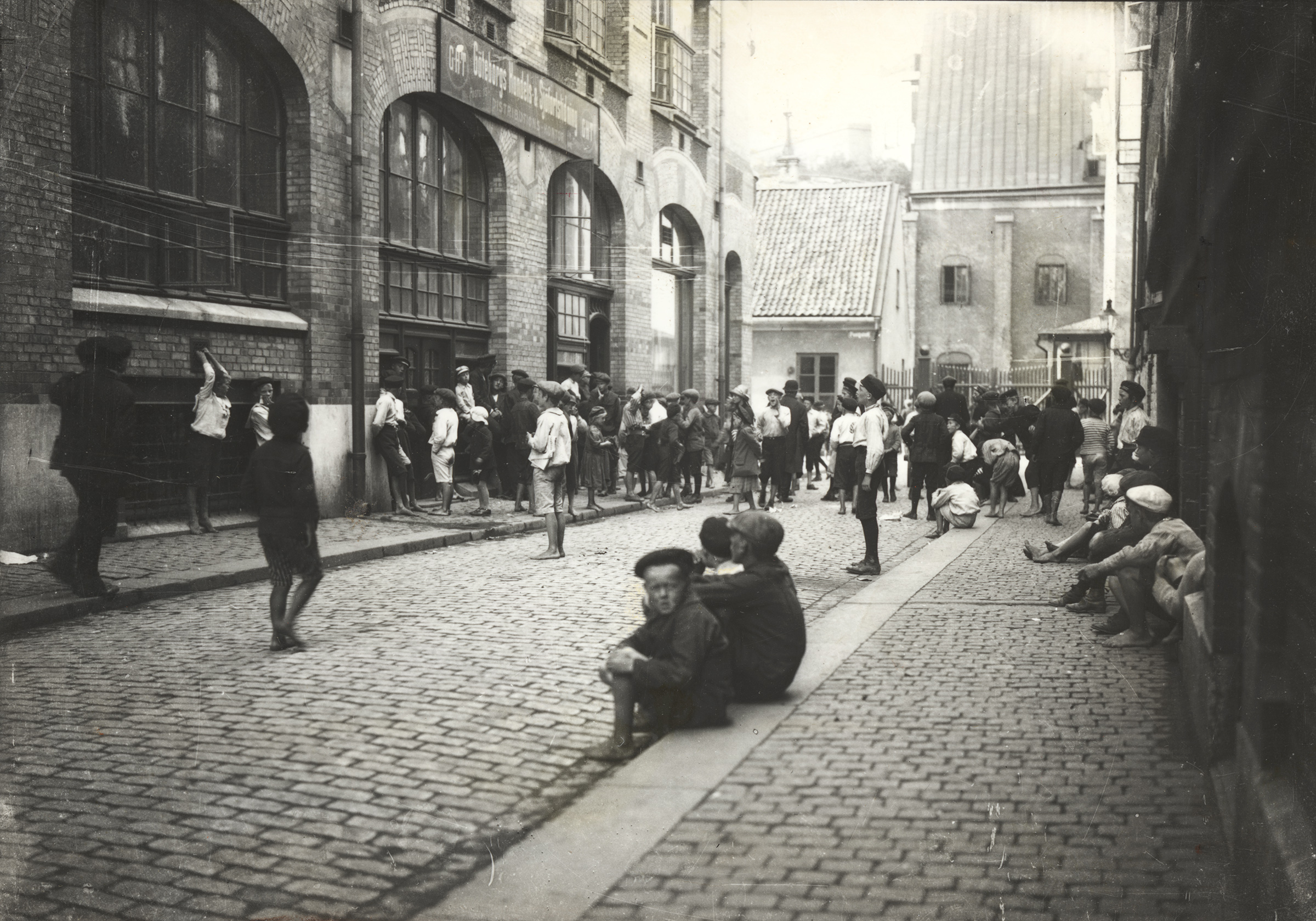 Springpojkar sitter och står på en trottoar i början av 1900-talet.