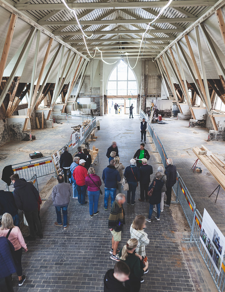 Människor som står i grupper i en stor öppen byggnad med träkonstruktion i taket